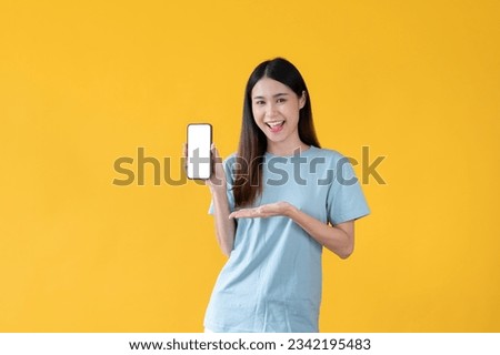 A beautiful and smiling young Asian woman is showing the white screen of a smartphone in her hand to the camera while standing against an isolated yellow background.