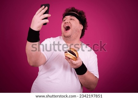 Funny fat man is engaged in fitness and and greedily eats a hamburger. Retro style. Pink background.