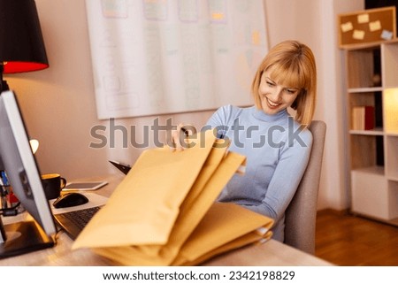 Woman small business owner sitting at her desk in home office, packing products for delivery; female entrepreneur packaging online store orders for shipping Royalty-Free Stock Photo #2342198829