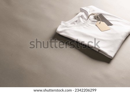 Folded white t shirt with tags with copy space on brown background. Fashion, clothes, colour and fabric concept.