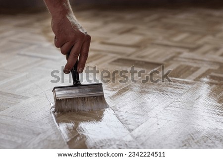 Hand of a man, worker oiling an authentic oak wooden floor  consiting of tiles with a big brush in a new cosy warm home environment. Finishing beautiful wood with protective oil Royalty-Free Stock Photo #2342224511