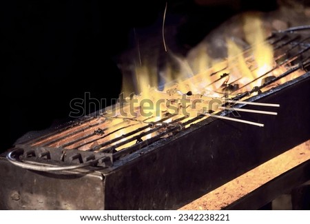 a photography of a grill with skewers on it and flames, there is a grill with skews on it with flames.
