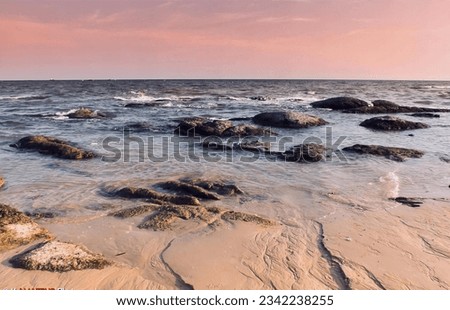 a photography of a beach with rocks and water at sunset, there is a bird that is standing on the rocks in the water.