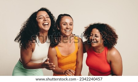 Cheerful group of three young, diverse female athletes celebrate their friendship and healthy lifestyle while wearing fitness clothing in a studio. Sporty young women laughing together. Royalty-Free Stock Photo #2342240457