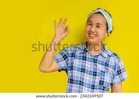 Asian woman making hand gesture ok, leaving space to put products or food menu.Isolated on yellow background.