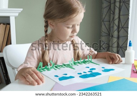 Cute child creating an applique with colored paper and glue. Concept of hobby and education