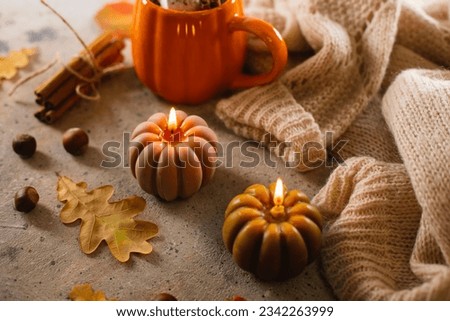 Burning candles shape of pumpking, mug with aiutumn drink, leaves and cinnamon. Autumn mood, hygge atmosphere.