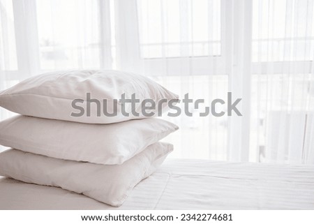 Stack of white soft pillows on comfortable bed sheet with window on background Royalty-Free Stock Photo #2342274681