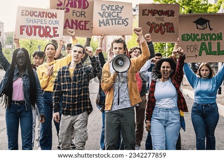 Multiracial Students Protesting for Education - Diverse group of young students marching, raising clenched fists and holding signs advocating for change in education. Royalty-Free Stock Photo #2342277859