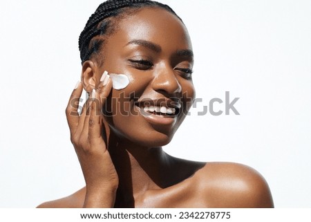 Beauty and skin care. Skincare hydration and oil balance. Portrait of African American woman with afro braids hairstyle is applying a cream smear on her face and standing against white background Royalty-Free Stock Photo #2342278775