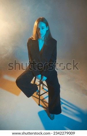 Portrait of a girl in a studio setting with smoke and colored light. The model is sitting on a chair. 