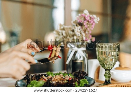 Pieces of meat and vegetables on a fork supported by a knife on the background of a plate with salad in a blue plate, which is on a table next to a wooden cutlery stand, a glass of water