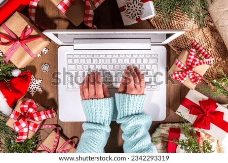 Person using laptop computer with Christmas gift boxes from above on wooden background. Notebook with woman hands with presents, fir tree and winter decor. Preparation for Christmas, New Year