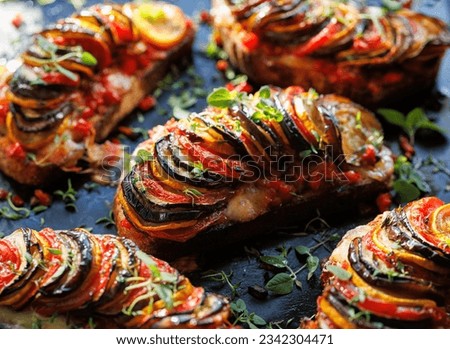Grilled sourdough bread open faced sandwich with sliced vegetables and mozzarella cheese sprinkled with fresh herbs on a black background, close up view. Tian sandwich Royalty-Free Stock Photo #2342304471