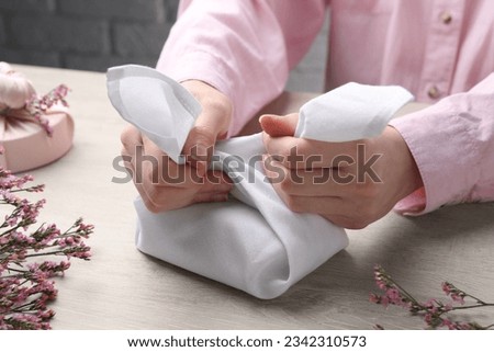 Furoshiki technique. Woman wrapping gift in white fabric at wooden table, closeup
