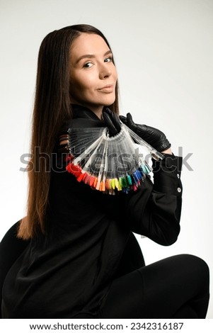 Beautiful darkhair woman nails master wearing dark uniform showing palette with nail polish colors samples, side view, white wall background. Advertising banner for beauty salons. Royalty-Free Stock Photo #2342316187