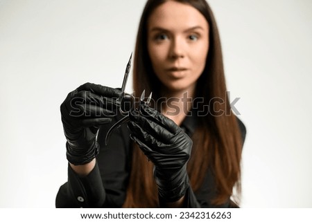 Darkhair attractive woman manicure master or nail care beautician holding sharp manicure tools. Nail care concept. White background Royalty-Free Stock Photo #2342316263