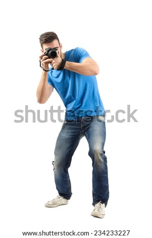 Bend or lean young man taking photo with dslr looking at camera. Full body length portrait isolated over white background.