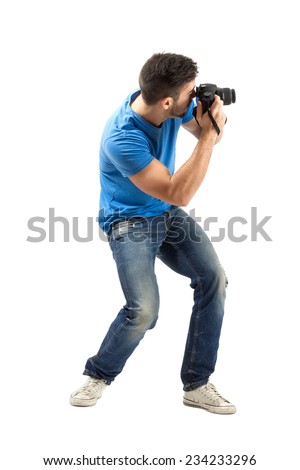 Bend young man taking photo with digital camera side view. Full body length portrait isolated over white background.