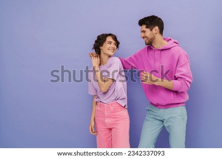 Young smiling couple wearing pastel clothes dancing isolated over purple studio background