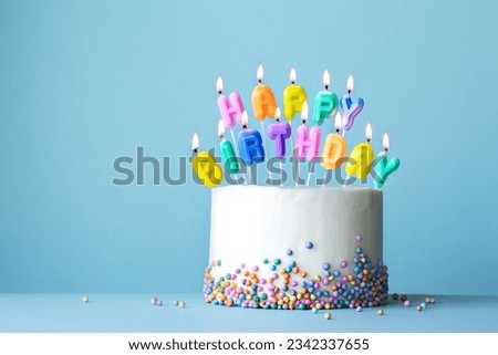 Colorful birthday cake with birthday candles spelling happy birthday against a blue background