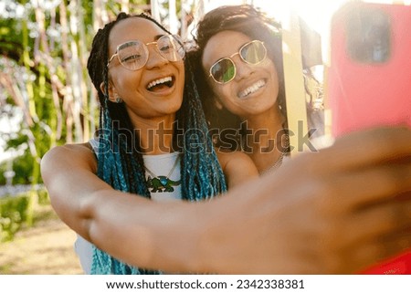 Two smiling carefree african american women taking selfie during party in summer park