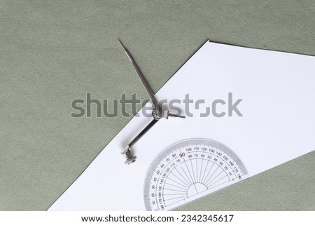 classic geometry instruments - compass (metal object) and protractor (semi circle plastic shape) on white and green paper
