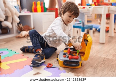 Adorable caucasian boy playing with tools toy sitting on floor at kindergarten Royalty-Free Stock Photo #2342358639