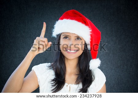 Closeup portrait of happy christmas woman, with red hat, pointing with index finger, aha i have an idea, positive human facial expression, isolated on grey black background. Emotions, signs, symbols