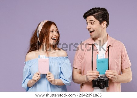 Two amazed traveler tourist woman man couple in shirt hold passport tickets look to each other isolated on purple background. Passenger travel abroad on weekends getaway. Air flight journey concept.