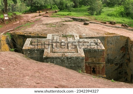 The cross-shaped Rock-hewn Church of Saint George surrounded by green grass and trees in Lalibela, Ethiopia Royalty-Free Stock Photo #2342394327