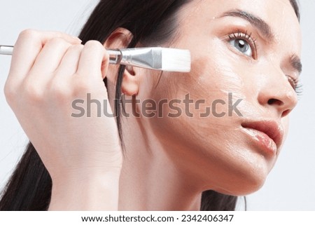 Young brunette woman applying moisturizing gel mask with brush on her face. Skin care, moisturizing and nourishing, anti-aging products and treatments Royalty-Free Stock Photo #2342406347