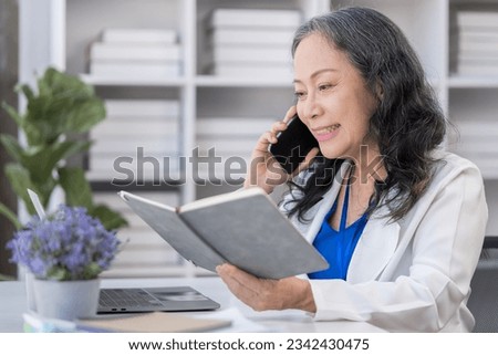 Positive middle age businesswoman having phone conversation and reading information on notebook.