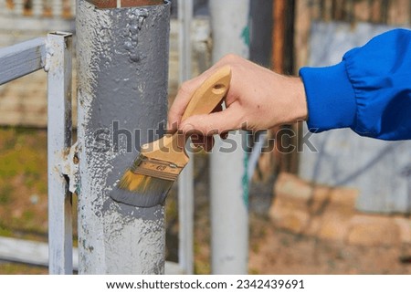 Anticorrosive painting of the fence,a man paints a fence in the yard with anti-corrosion paint