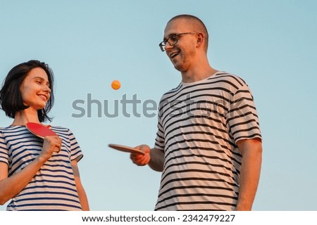 Beautifull couple holding ping pong or table tennis paddles with ball on sky background .Striped t-shirt. Concept of sport and active life. 