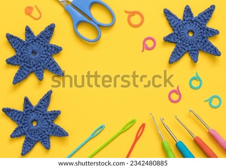 Bright colorful crochet tools with blue crochet snowflakes on a yellow background. Top view. Copy space.