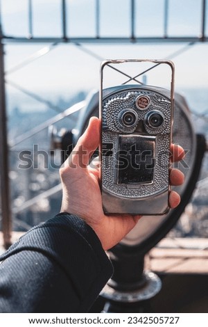 A person taking a picture of binoculars with a view to New York skyline with a phone