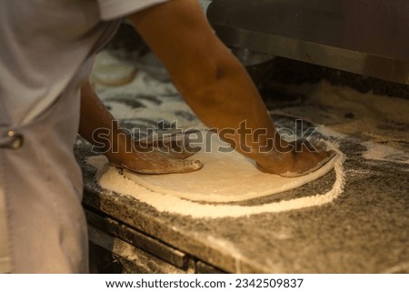 A person preparing pizza dough, a man rolling out the dough on a stone table, kneading the dough before baking