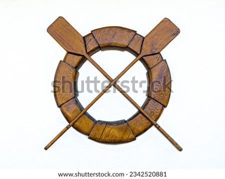 Decorative wooden life preserver and boat oars symbolizing water rescue. Royalty-Free Stock Photo #2342520881