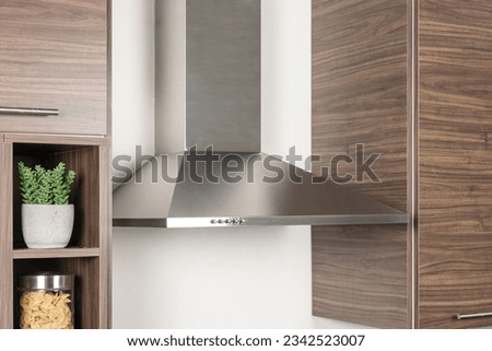 A Stainless Steel kitchen hood beside a melamine wooden kitchen cupboard set in the corner of a room, close up Royalty-Free Stock Photo #2342523007