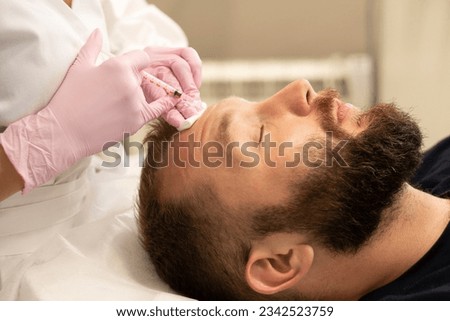 Men's cosmetology. Cosmetologist makes botulinum toxin beauty injection procedure in forehead wrinkles of handsome young man with beard in beauty salon. Royalty-Free Stock Photo #2342523759
