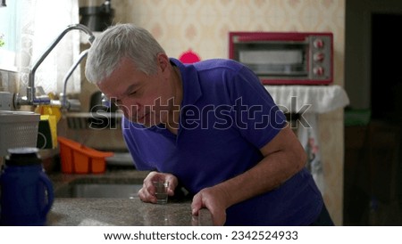 Drunk senior struggling with alcoholism leaning on kitchen sink at home, unhealthy behavior lifestyle in old age. Substance abuse concept Royalty-Free Stock Photo #2342524933