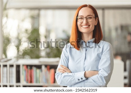 Portrait of beautiful smiling confident businesswoman, manager, CEO holding arms crossed looking at camera. Happy smart university student wearing eyeglasses standing in modern library, education Royalty-Free Stock Photo #2342562319