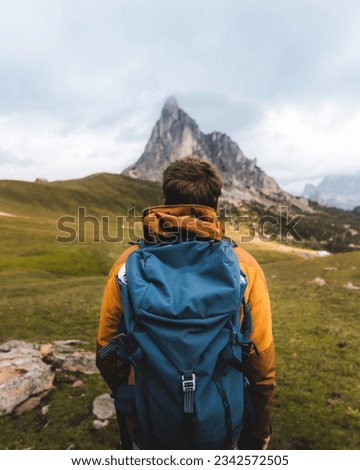 Young man with a blue mountaineering backpack is observing terrain during his hike in the Alps, Italian Dolomites. Royalty-Free Stock Photo #2342572505
