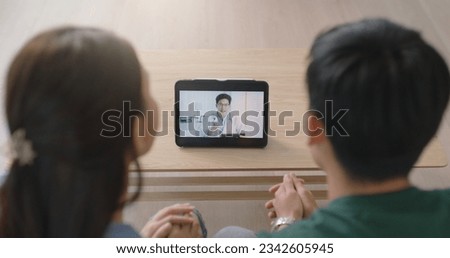 Young married asia people prepare pregnant plan checkup preconception consult at home sofa. Clinic app illness screen on online advice doctor remote exam telemedicine video call talk on tablet phone. Royalty-Free Stock Photo #2342605945