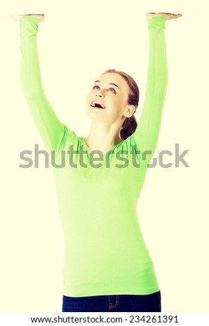 Smiling young woman is holding something abstract above her head. Happy girl with raised hands. Isolated on white background.