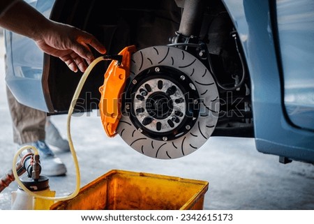 Car mechanic or serviceman disassembly and checking a disc brake and asbestos brake pads for fix and repair problem at car garage or repair shop Royalty-Free Stock Photo #2342615173