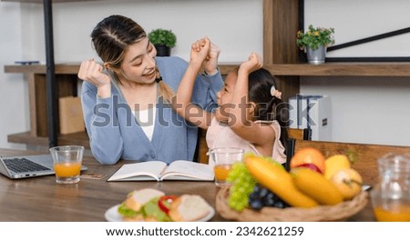 Asian young female mother and little cute girl daughter sitting smiling learning studying doing homework online via laptop notebook computer drinking orange juice eating sandwich together at home.