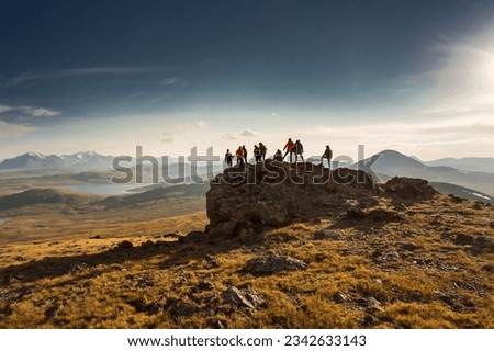 Big diverse group of hikers silhouettes stands at mountain top and looks at sunset