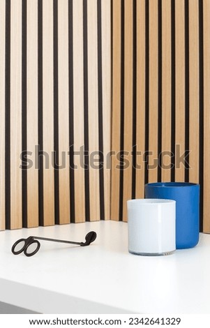 Candles and a wick trimmer on a wooden table, with natural wood slat background. Neutral colors and natural lighting with occasional pops of blue and orange.
